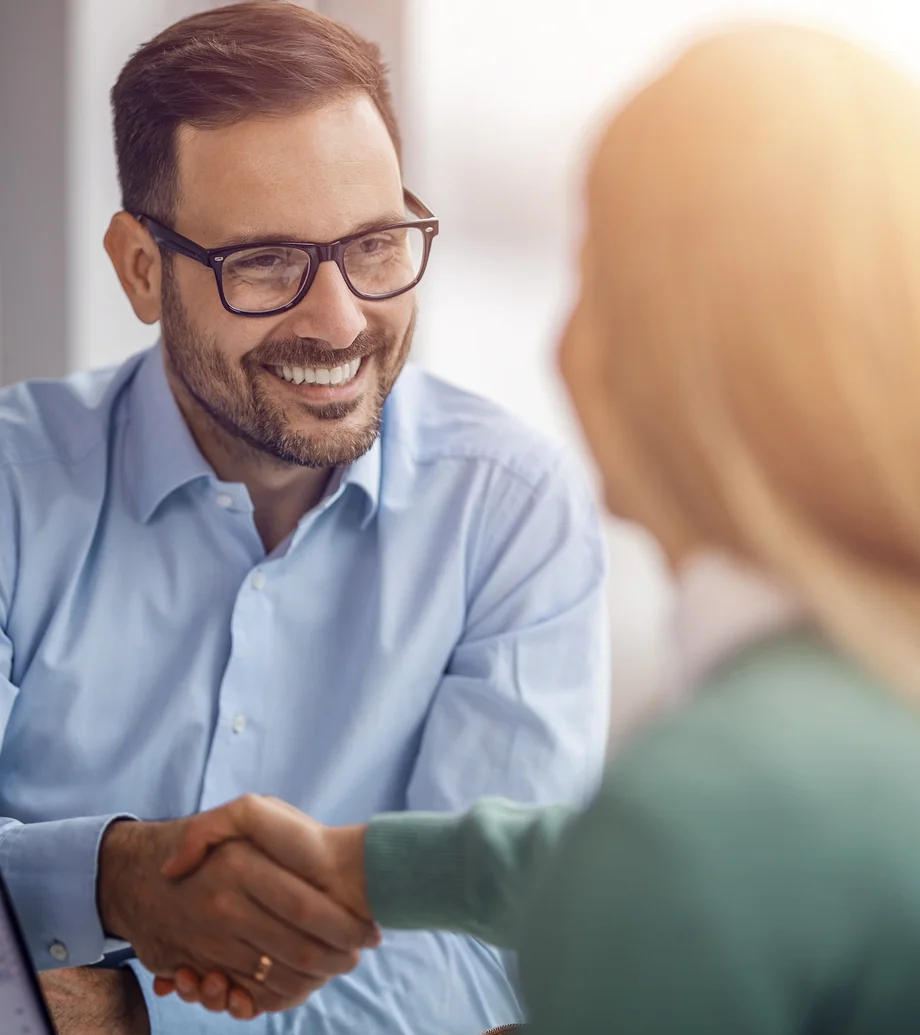 Foto einer Beratungssituation: Ein Mann mit Brille und dunklen Haaren schüttelt einer blonden Frau die Hand.