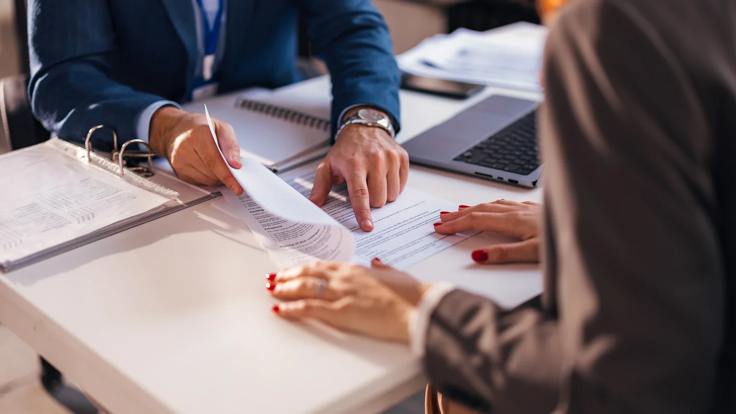 Foto eines Close-ups einer Beratungssituation: Es sind Hände zu sehen, die gerade einen Vertrag durchgehen.